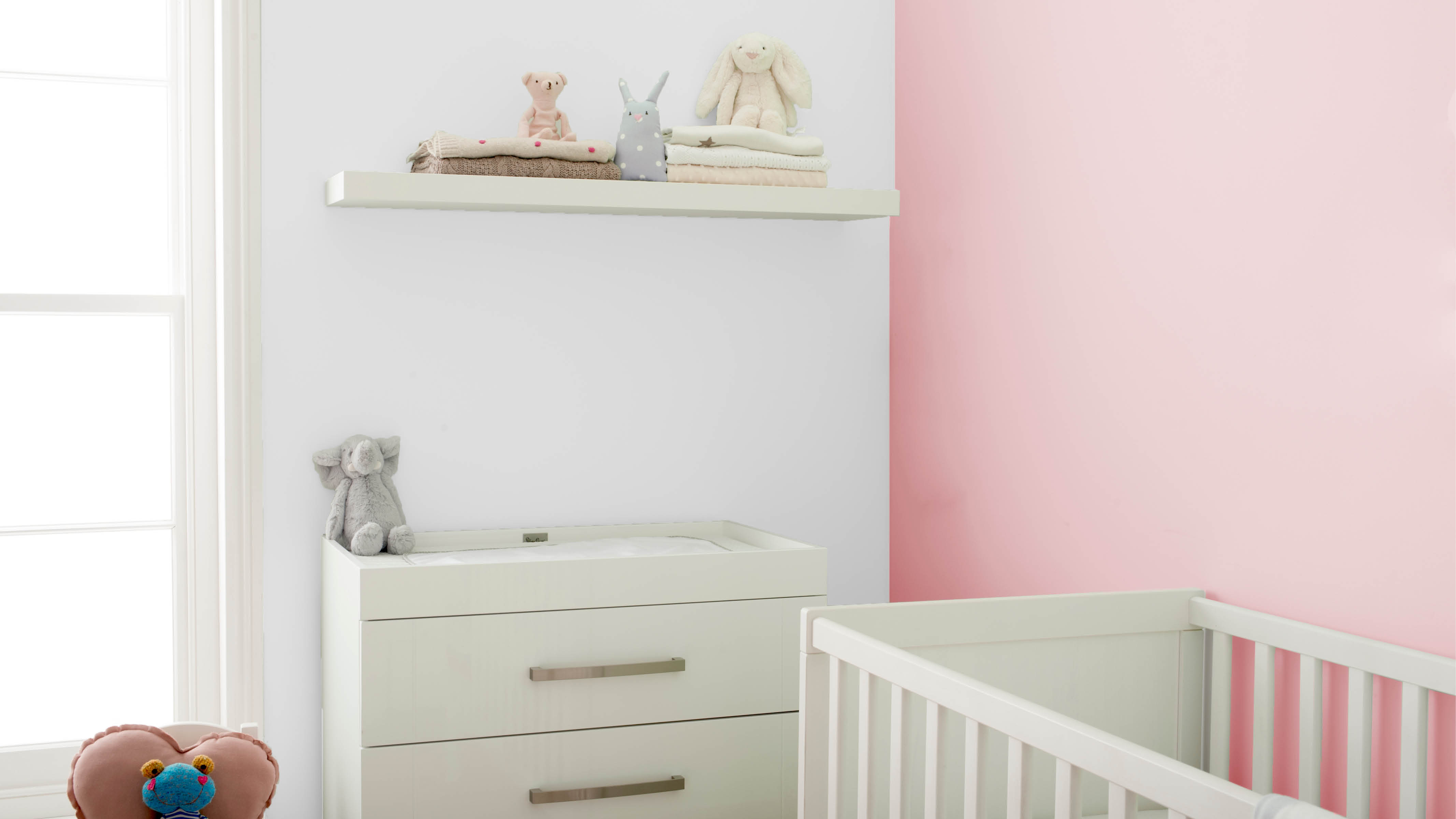 Lyserødt børneværelse med væghylder Et hvidt skab og et sæt væghylder er et godt sted at opbevare bleer og andet udstyr til babypleje.